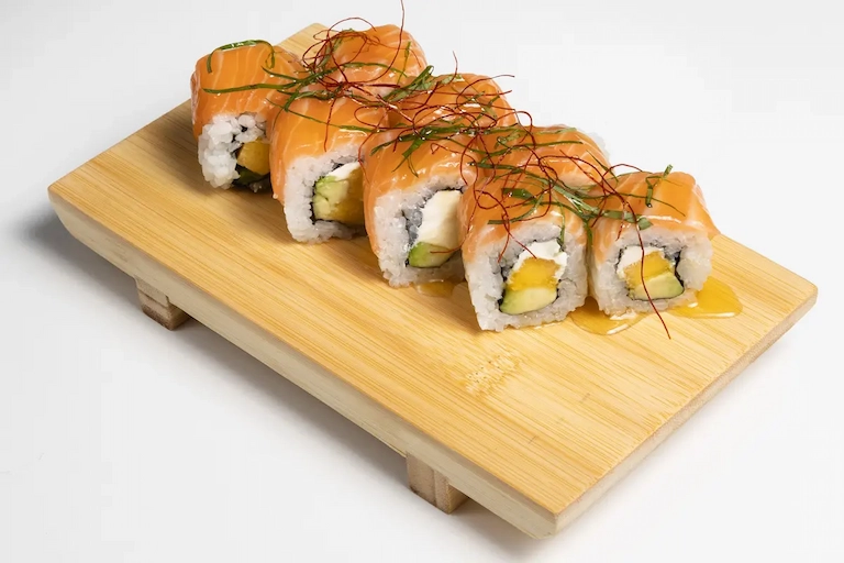 Chef de Amaru Sushi Bar flambeando sushi en la barra, con llama visible sobre piezas de salmón o atún, en un entorno moderno y cuidado