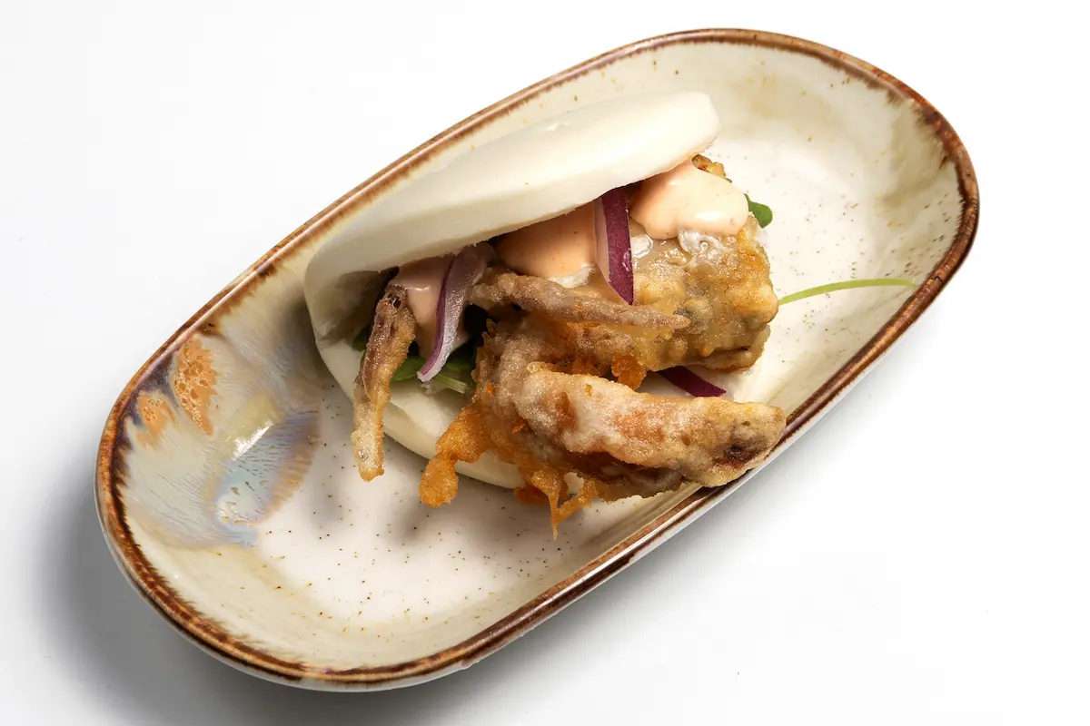 Bao de cangrejo de Amaru Sushi Bar relleno de cangrejo crujiente en tempura, con ensalada asiática, salsa cremosa y pan bao al vapor, servido en presentación gourmet