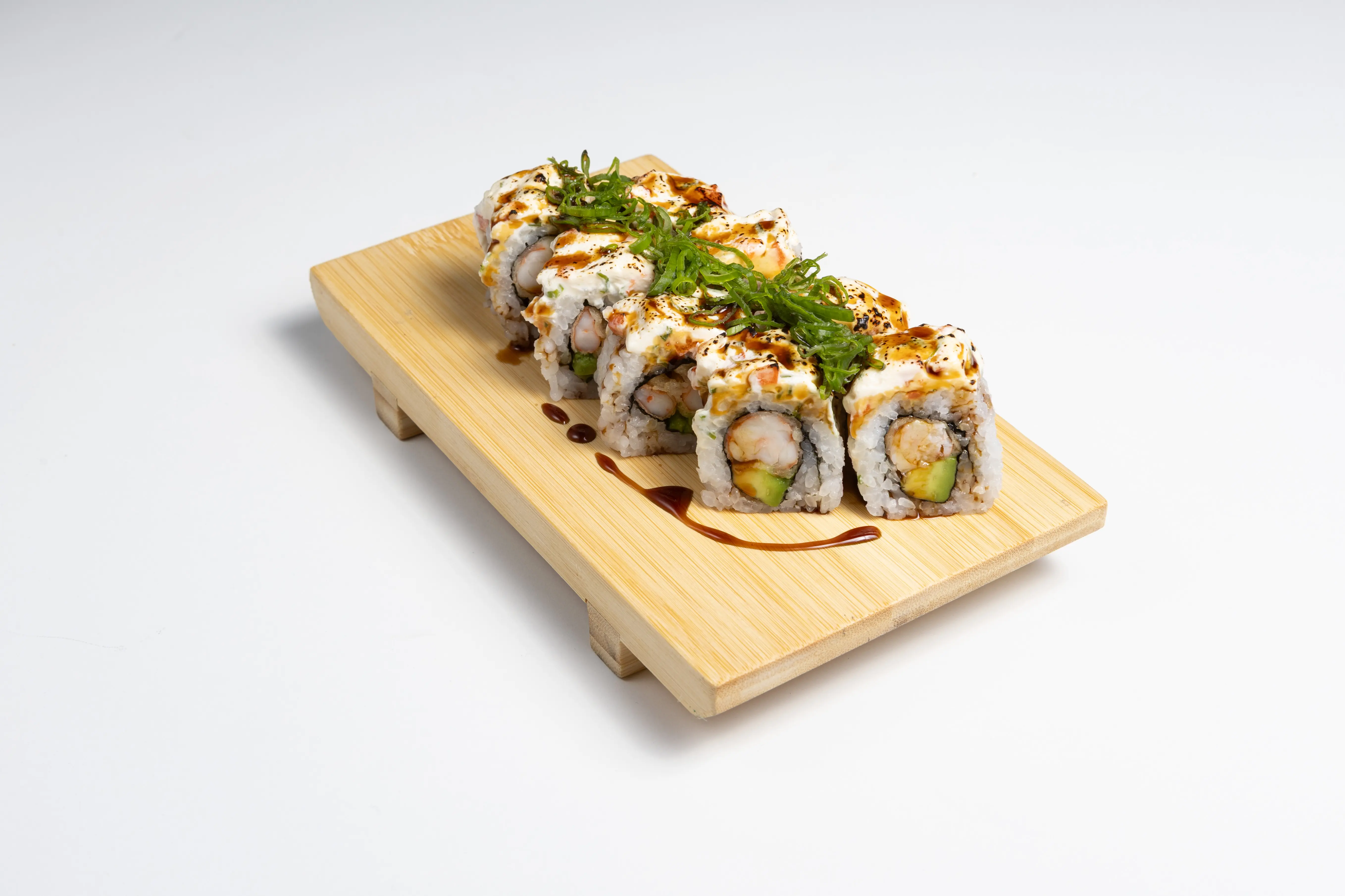 Valpo Roll de Amaru Sushi Bar con gamba furai y aguacate, cubierto con crema nikkei flambeada y salsa teriyaki, presentado en plato gourmet